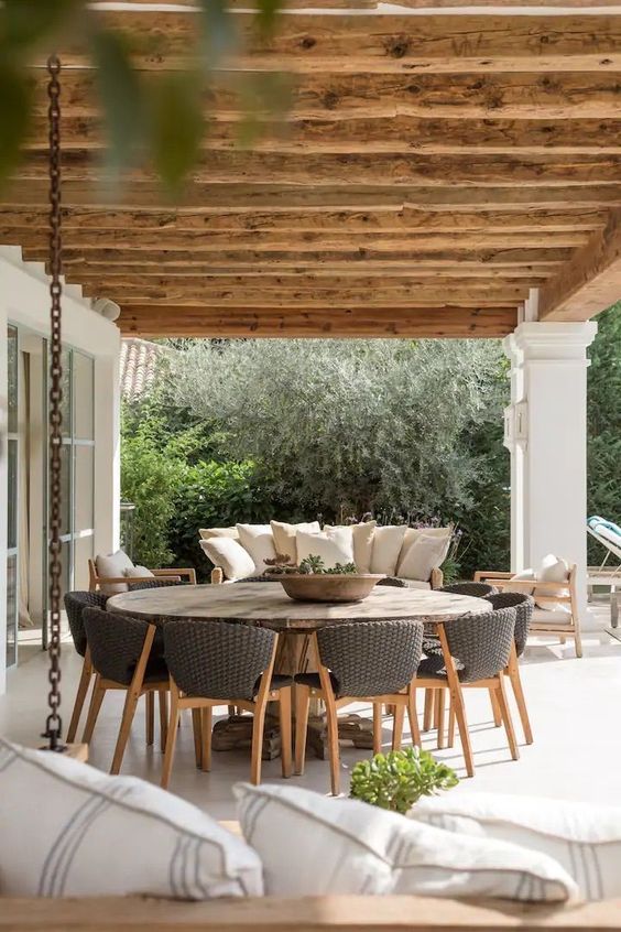 a modern farmhouse terrace with a round table, wicker chairs, a sofa and chairs and some greenery is a lovely space