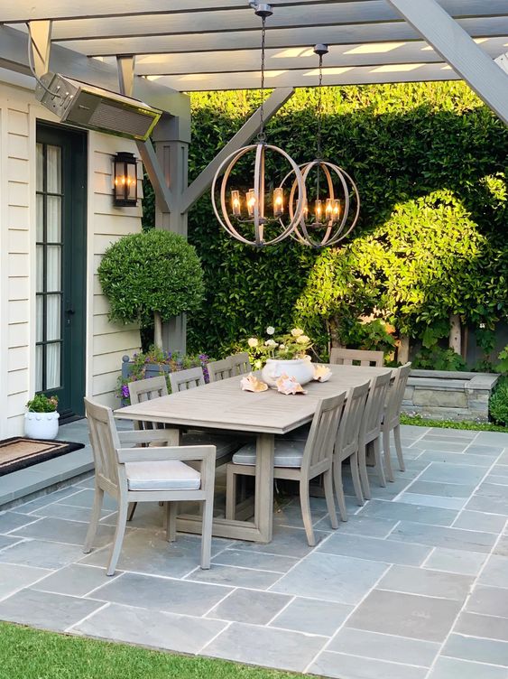 a modern farmhouse terrace with a stained table and chairs, sphere pendant lamps, potted greenery and blooms is a welcoming space
