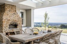 a modern farmhouse terrace with a stone hearth, a kitchen, a stained trestle table and wicker chairs is amazing