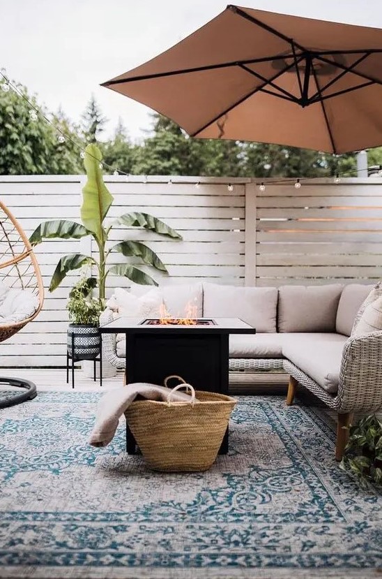 a modern farmhouse terrace with a wicker sectional, a fire pit, a rattan chair, an umbrella, potted plants is a lovely space