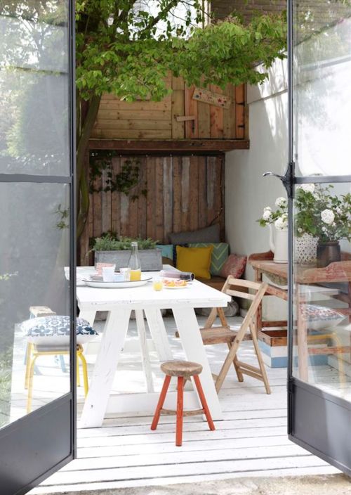 a modern farmhouse terrace with stained and painted furniture, bright pieces, potted plants and blooms is a cozy space