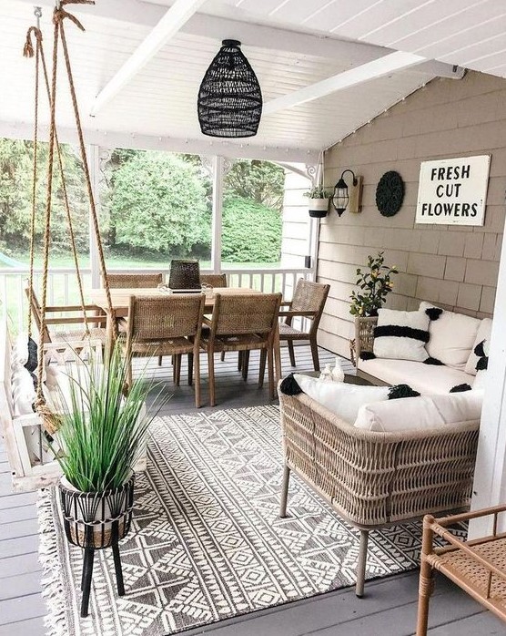 a modern farmhouse terrace with wicker and wood furniture, a suspended daybed, neutral textiles and potted plants