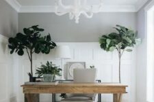 a modern home office with a white chandelier, a wooden trestle desk, a white chair, a printed rug and statement plants