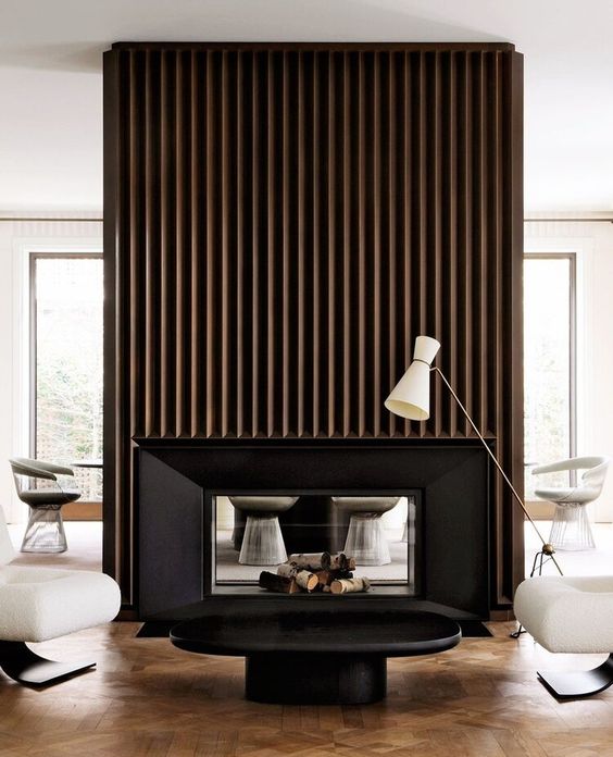 A modern living room with a double sided fireplace and a reeded surround, creamy chairs, a black coffee table and a floor lamp