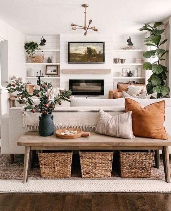 a modern neutral farmhouse living room with built-in shelves, a fireplace, a neutral sofa and amber chairs, a wooden bench and baskets
