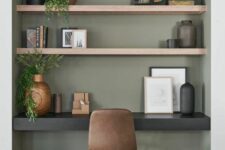 a modern niche painted olive green, with built-in shelves and a black desk, some decor and greenery, a brown leather chair and artwork