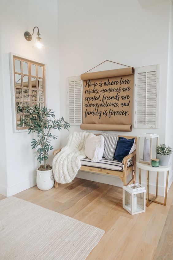 a modern rustic entryway with a wooden bench and pillows, candle lanterns and a sign, a potted plant and a framed mirror