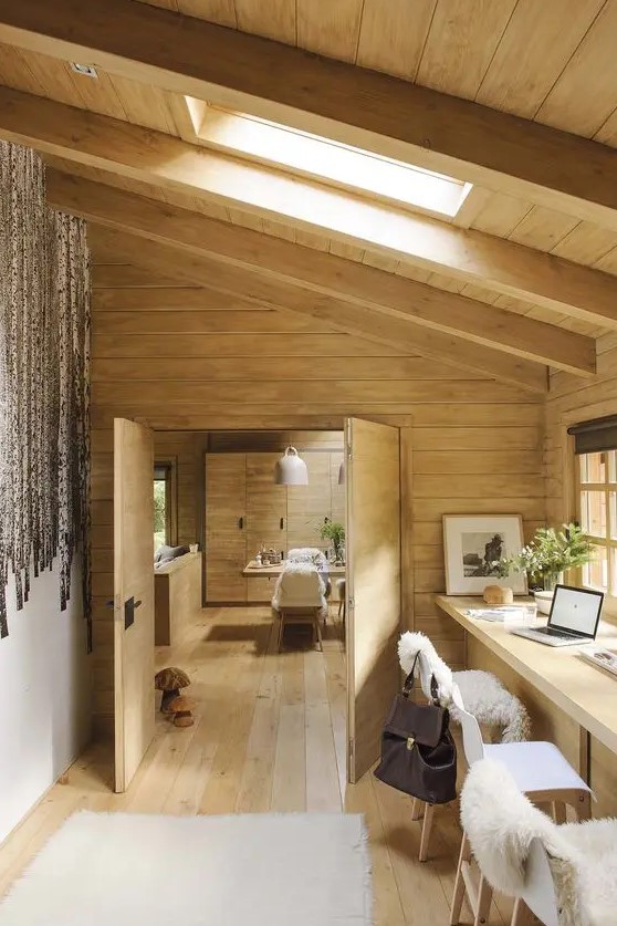 a modern rustic home office with a shared desk, a couple of chairs, an attic ceiling with a skylight and soem faux fur