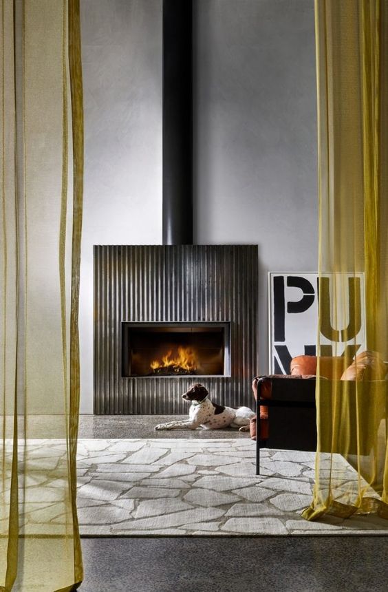 a modern space with a fireplace and a fluted surround, an orange leather chair, a printed rug and some cool decor