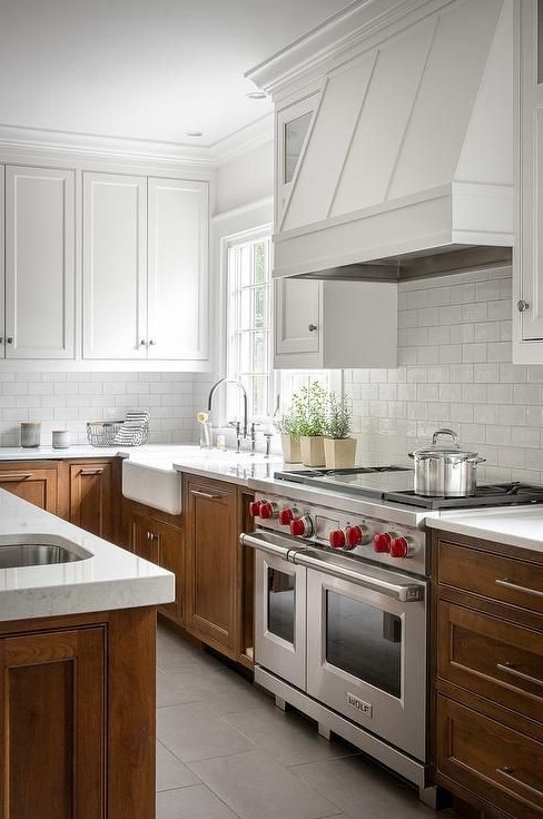 A modern two tone kitchen with white upper and stained lower cabinets, white stone countertops, a metal hood painted white is great