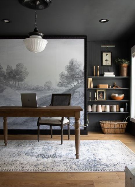 a moody modern farmhouse home office with black walls and a ceiling, a stained desk and a neutral chair, open shelves and a pendant lamp