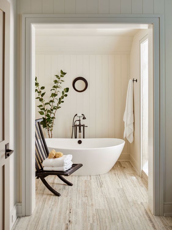a neutral and welcoming modern farmhouse bathroom with shiplap walls, a neutral floor, an oval tub, a lack folding chair, black fixtures
