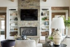 a neutral barn living room with a built-in fireplace, neutral seating furniture, wooden beams, a metal chandelier and baskets
