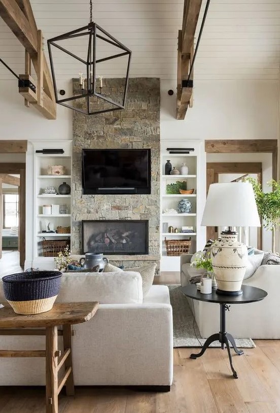 a neutral barn living room with a built-in fireplace, neutral seating furniture, wooden beams, a metal chandelier and baskets