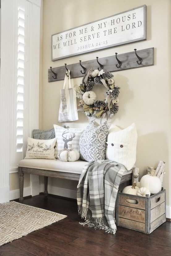 a neutral farmhouse entry with a large sign, a box with pumpkins, printed pillows, a pinecone and pumpkin wreath and a plaid blanket