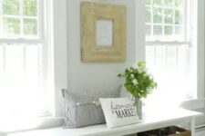 a neutral farmhouse entryway with an artwork, decorative plates, a bench, wooden boxes for storage and a striped pillow