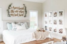 a neutral farmhouse space with an upholstered bed, a sign on the wall, a vintage chandelier, a wooden bench and a gallery wall