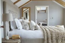a neutral modern country bedroom done in grey, with wooden beams and an upholstered bed, a wooden chest and neutral bedding