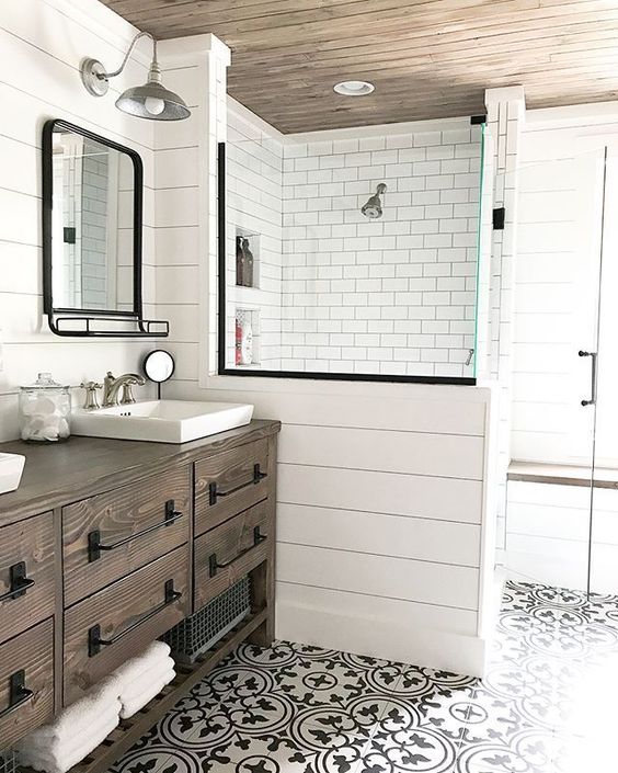 A neutral modern farmhouse bathroom with a shower space, a dark stained timber vanity, a printed tile floor, black hardware and vintage lamps