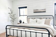 a neutral modern farmhouse bedroom with a shiplap accent wall, a wrought bed with neutral bedding, a stained bench and a printed rug