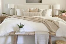 a neutral modern farmhouse bedroom with an upholstered bed with neutral bedding, a stained bench, stained nightstands, a basket and some decor