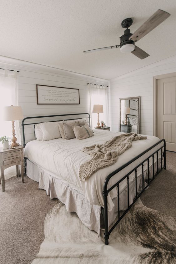 a neutral modern farmhouse bedroom with shiplap walls, a wrought bed, stained nightstands, layered rugs and a sign on the wall