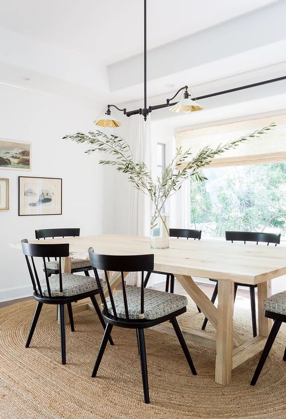 a neutral modern farmhouse dining room with a stained table and black chairs, a gallery wall and a chandelier