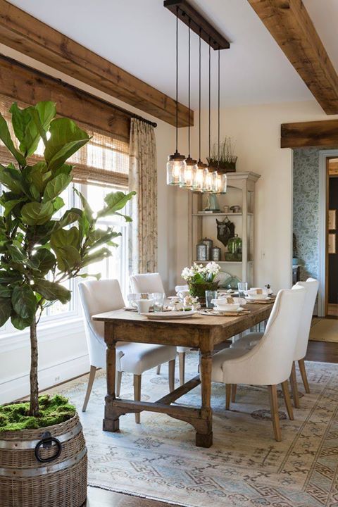 a neutral modern farmhouse dining room with a vintage stained table, neutral chairs, pendant lamps, some textiles and greenery