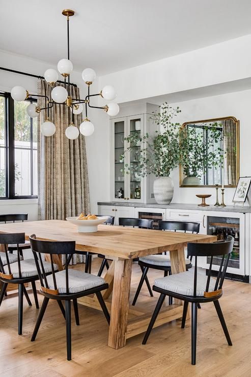 a neutral modern farmhouse dining space with a white storage unit, a stained table, black chairs and a chandelier
