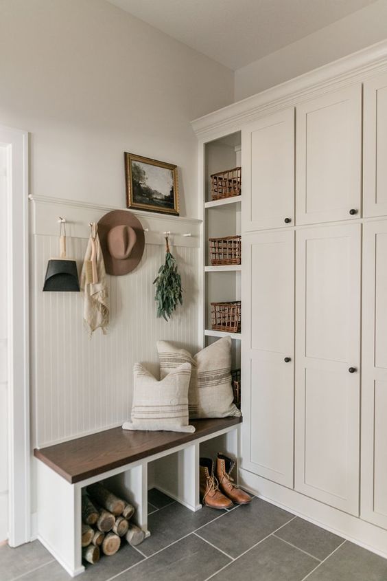 A neutral modern farmhouse entryway with a large storage unit, a built in bench, some baskets and a rack