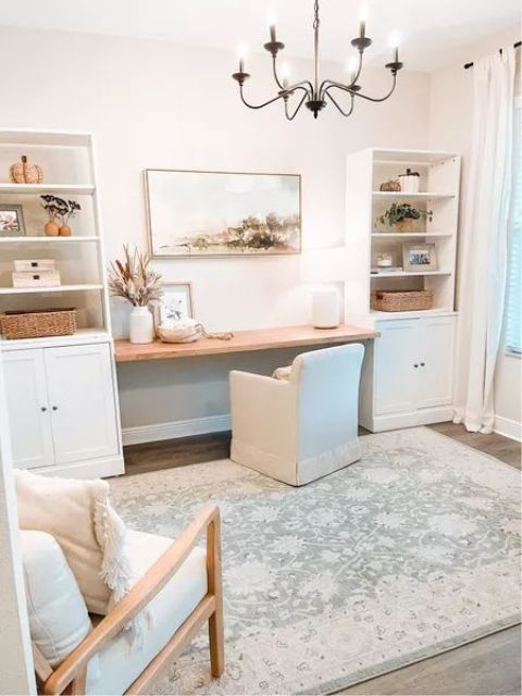 A neutral modern farmhouse home office with bookcases, a built in desk, white chairs, a chandelier and a boho rug