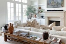 a neutral modern farmhouse living room with built-in shelves, a fireplace, a creamy sofa, a bench as a coffee table and a chandelier