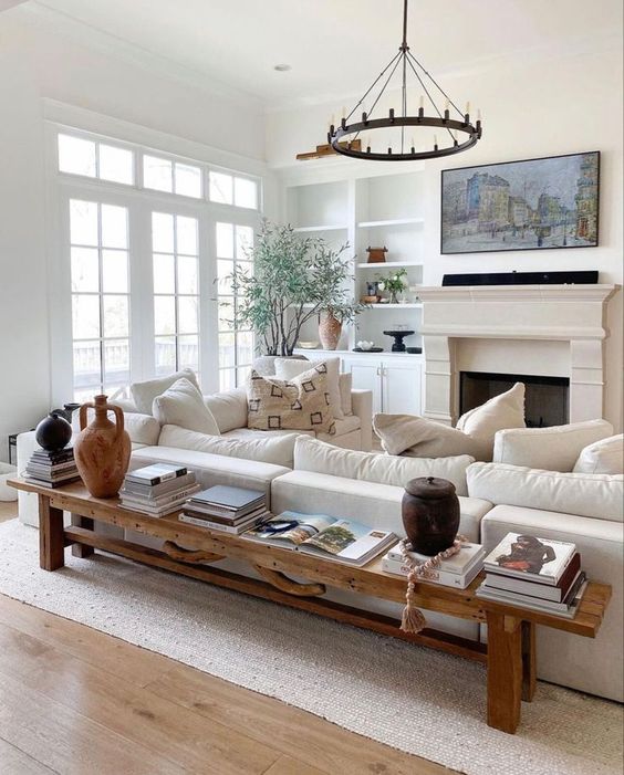 A neutral modern farmhouse living room with built in shelves, a fireplace, a creamy sofa, a bench as a coffee table and a chandelier