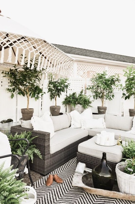 a neutral modern farmhouse meets boho terrace wiht dark wicker furniture, potted plants, neutral upholstery and tassels