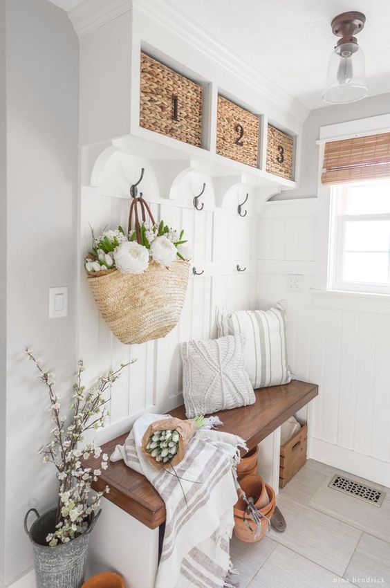 A neutral modern farmhouse mudroom with a built in bench and baskets, lots of blooms and greeneyr, some pillows