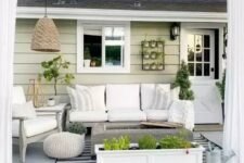 a neutral modern farmhouse outdoor living room with white upholstered furniture, a fire pit, potted greenery, a pendant lamp and neutral textiles