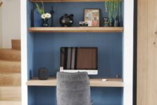 a niche painted blue with built-in shelves and a desk, some lovely decor, a PC and a grey chair is a cool solution