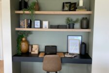 a niche painted olive green, with built-in shelves and a black desk, a taupe chair, some decor and potted greenery