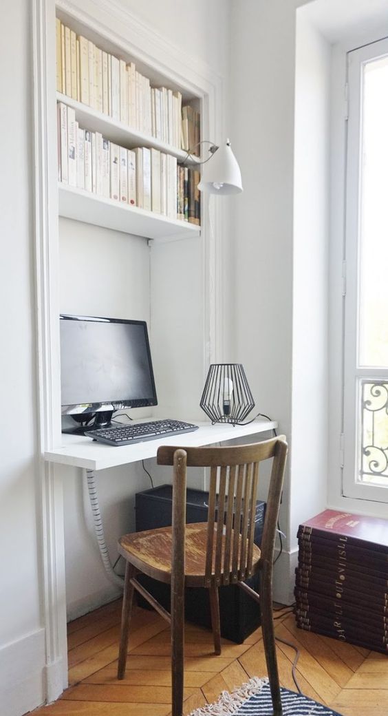 A niche with built in shelves and a desk, books, a sconce and a PC, a vintage stained chair