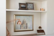 a niche with built-in shelves and a desk plus a retracting part, books, artwork, vases and a copper table lamp