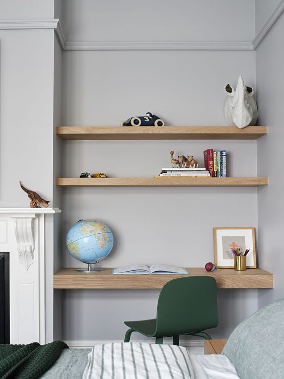 A niche with built in shelves and a desk, some books, photos, decor and a globe and a green chair