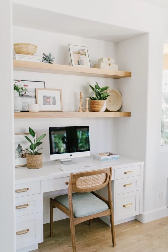 A niche with built in shelves and a desk with storage drawers, with decor, potted greenery and a comfy chair