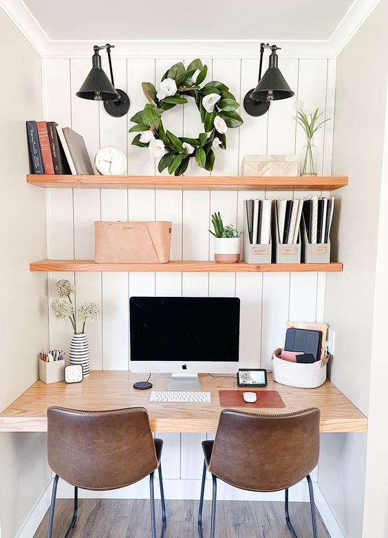A niche with shiplap, built in shelves, a desk, potted greenery, black sconces, books and brown leather chairs