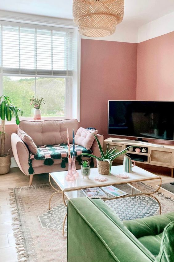 a pink living room with a TV on a TV unit, a pink chair, a green sofa, a tiered coffee table and a printed rug