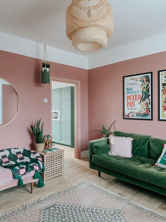a pink living room with a green velvet sofa, a pink chair with a green blanket, a round mirror, a woven pendant lamp