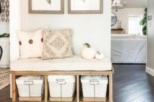 a pretty modern farmhouse entryway with a wooden bench and baskets, some pillows and pumpkins and a bit of art