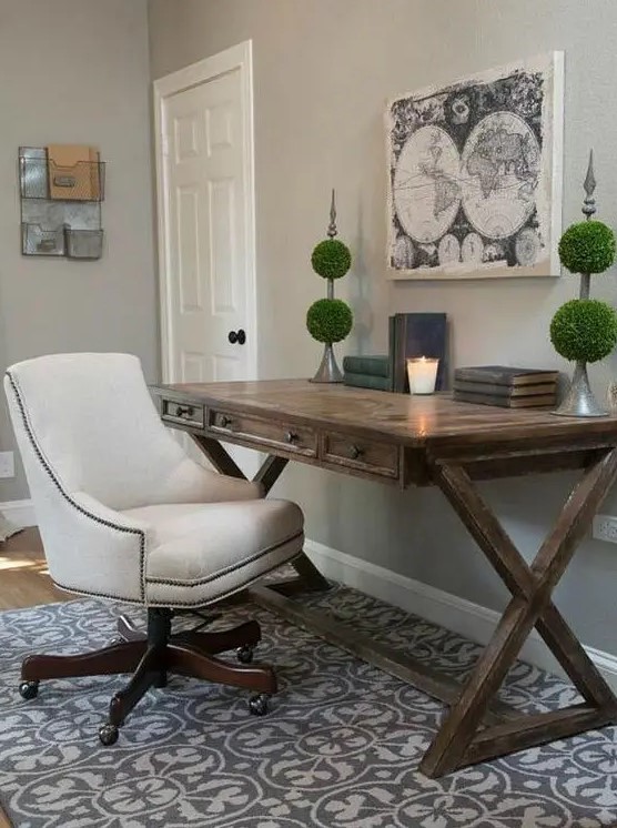 a rustic home office with a trestle desk, a printed rug, green topiaries, a white chair on casters is elegant