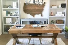 a rustic home office with open storage units, a wooden trestle desk, a printed rug and a state artwork on the wall