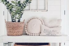 a serene modern farmhouse entryway with a white bench, a vintage window frame, a potted plant and some pillows