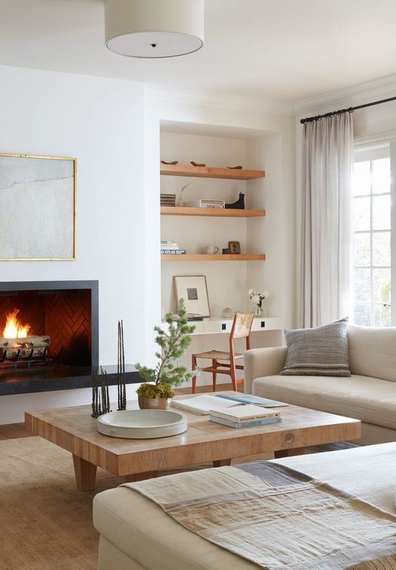 A serene modern farmhouse living room with built in shelves, a fireplace, a low coffee table, creamy sofas and neutral textiles